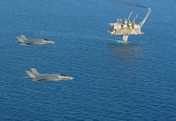 alt="To F-35 jagerfly flyr over en oljeplattform "