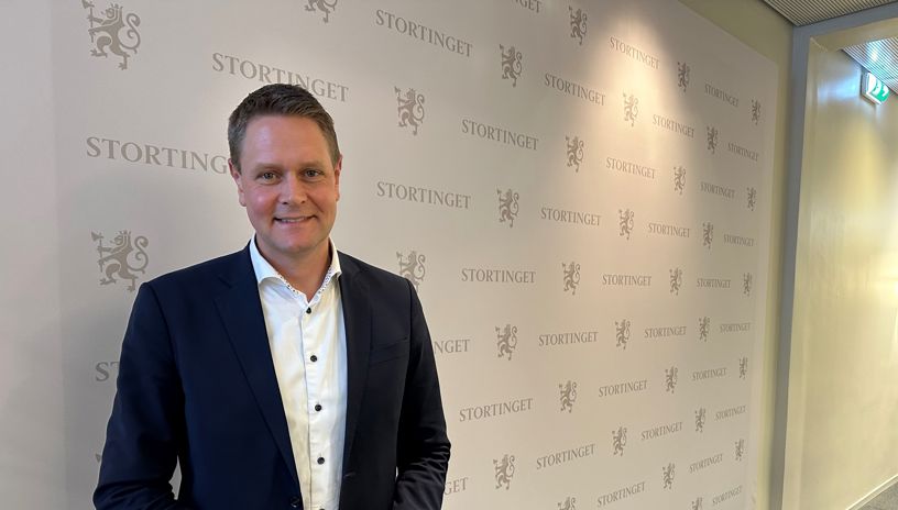 Harald Solberg foran en hvit pressevegg med Stortingets logo 