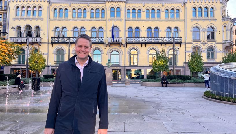 Harald Solberg smilende utenfor det gule komitébygget tilhørende Stortinget. 