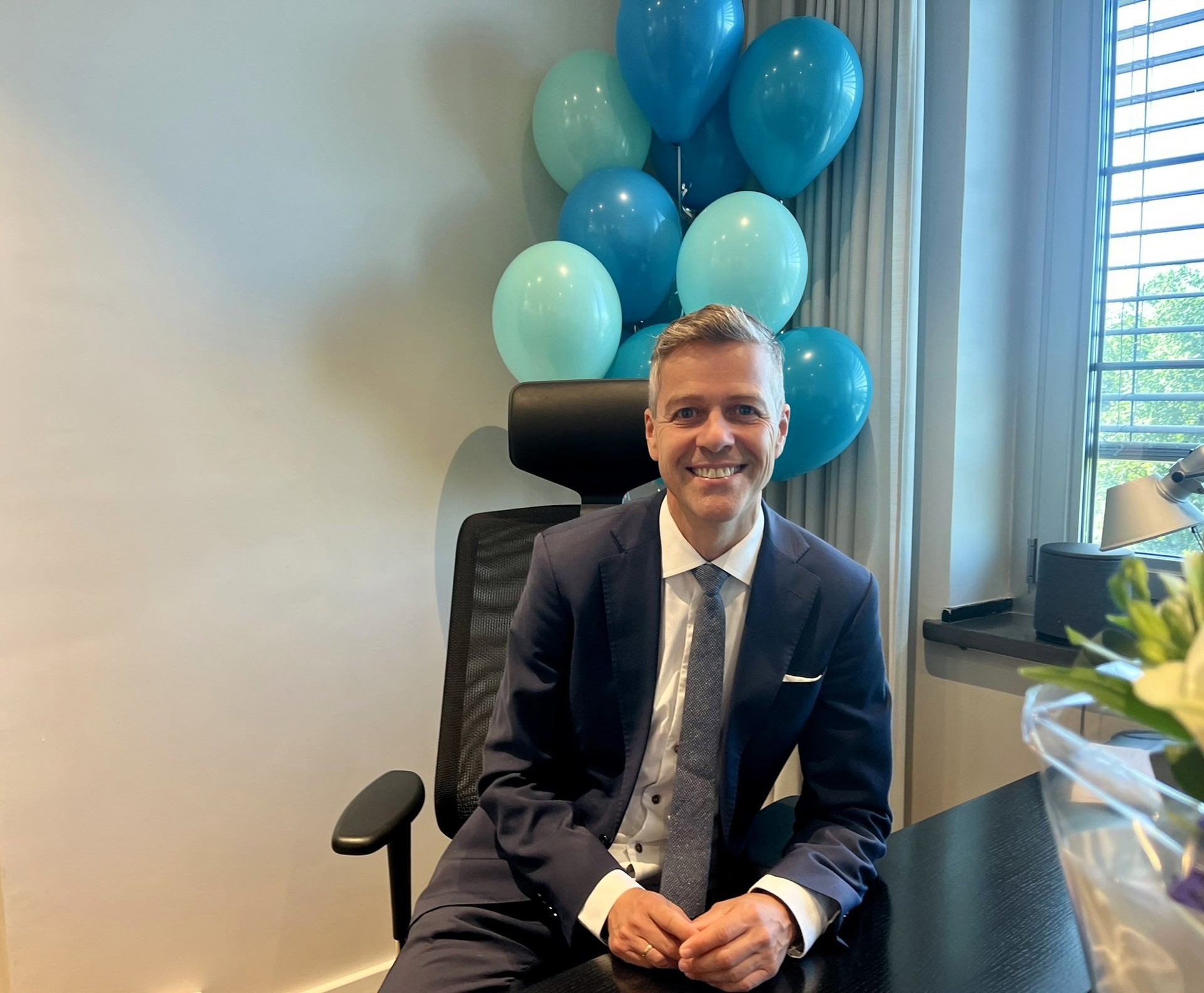 Knut Arild Hareide by his desk. In the background balloons in the colours of the NSA 