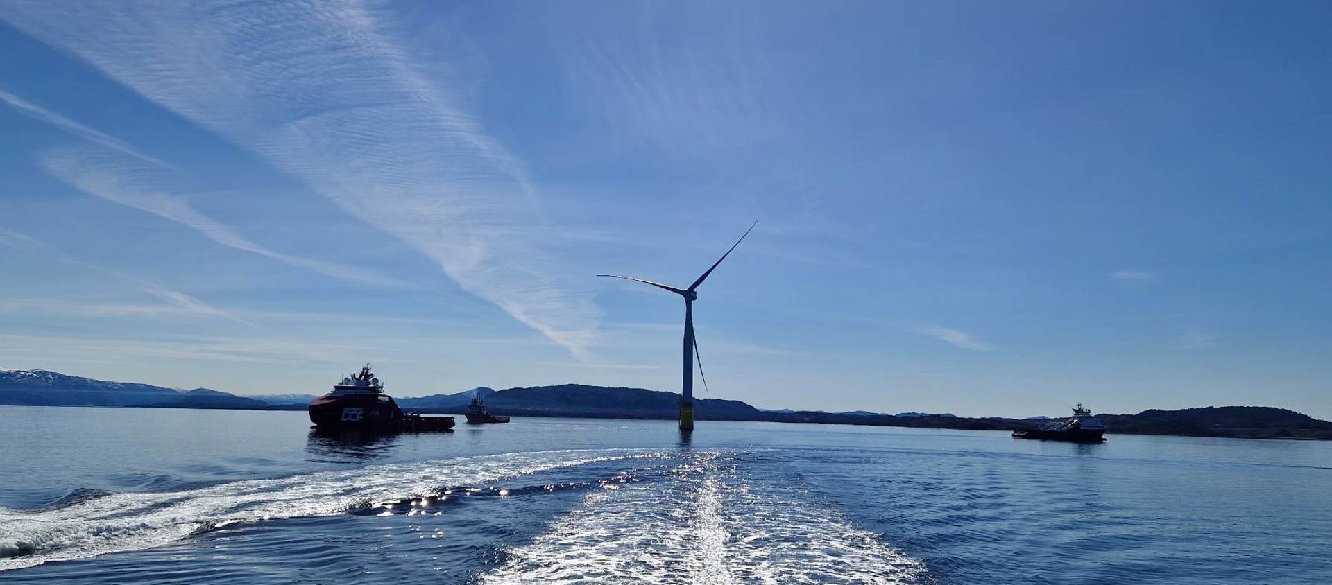 fra hywind tampen, to offshoreskip og en vindturbin i motlys 