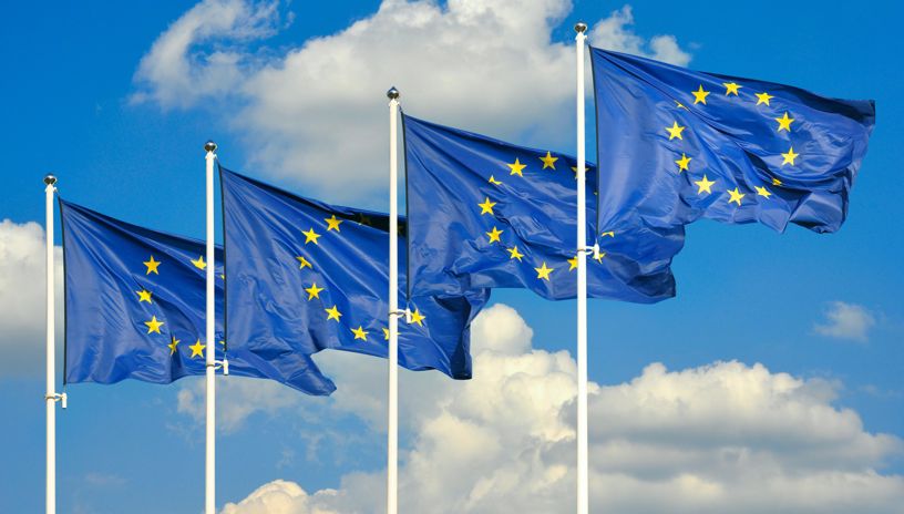 Four flagposts with EU flags against a clear blue sky 