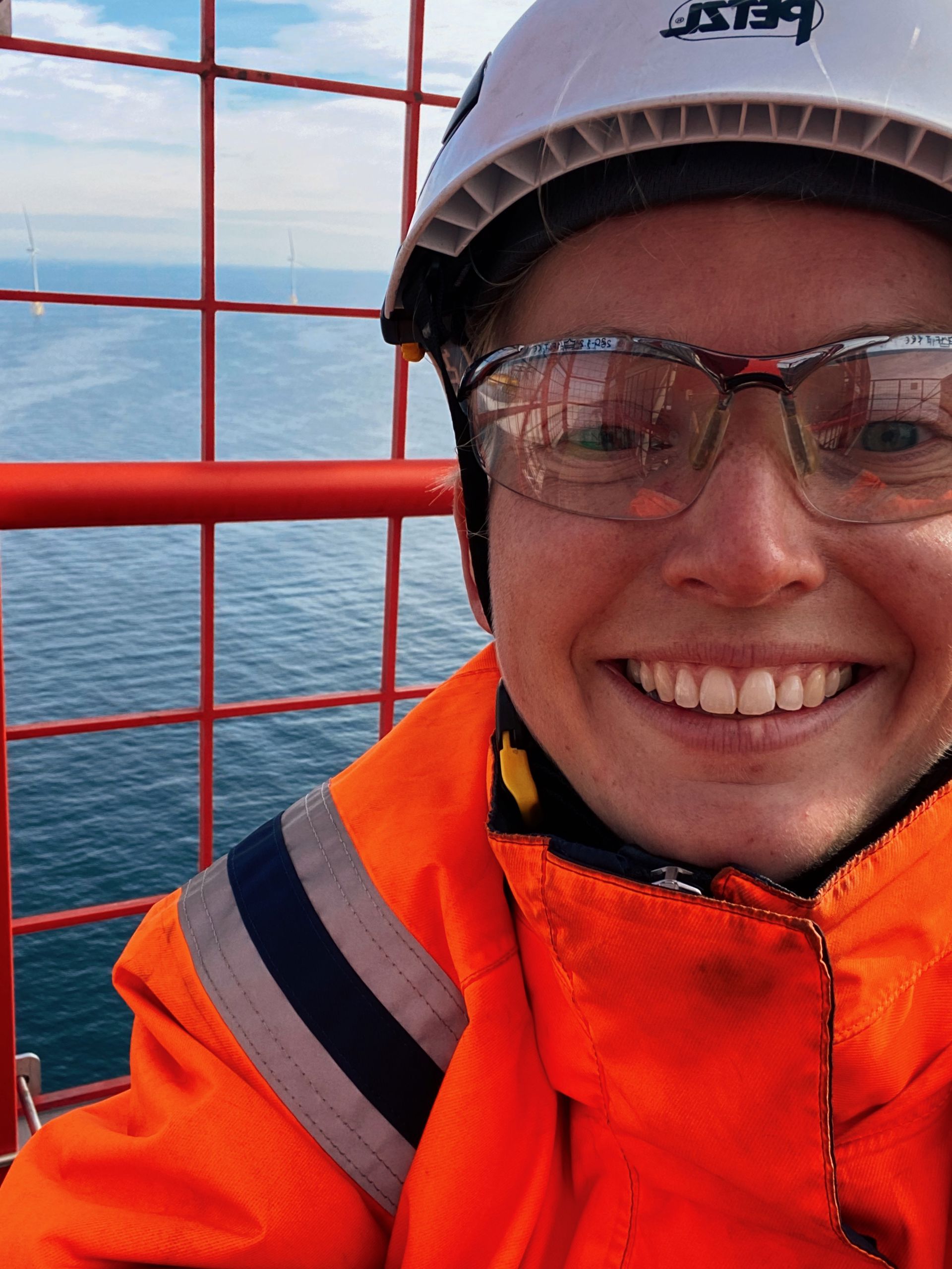 Selfie - Mari Storusl i toppen av en vindturbin uført orange arbeidsklær, hjelm og briller.