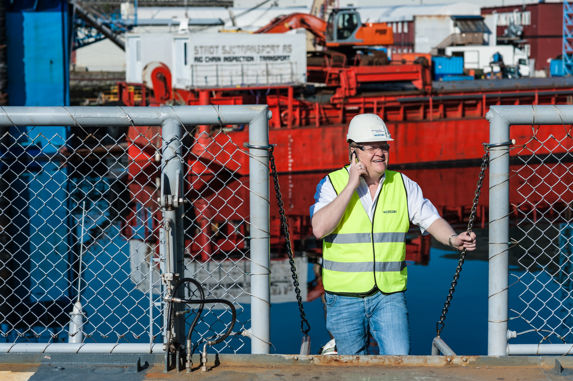 Geog Matre i telefonen iført regleksvest med skip i bakgrunnen. 