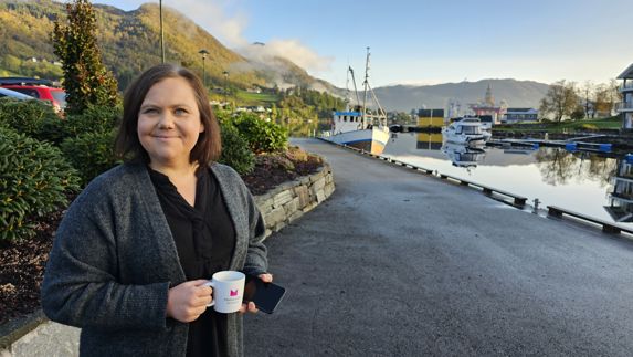 Kari Aakra med kaffekopp i hånden på kaia i Ølensvåg 
