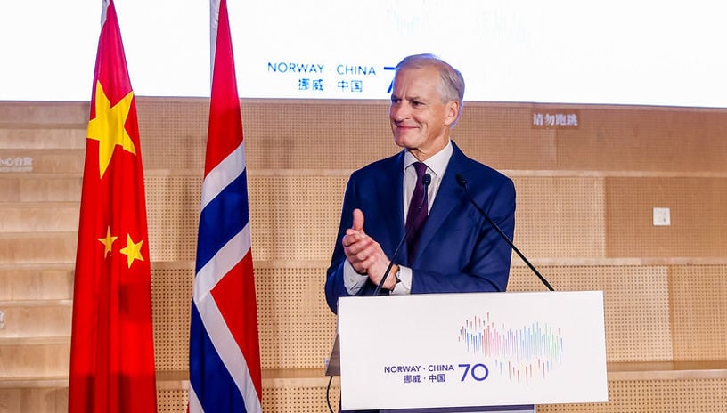 Statsminister Jonas Gahr Støre på talerstolen i Kina, med kinesisk og norsk flagg til venstre.