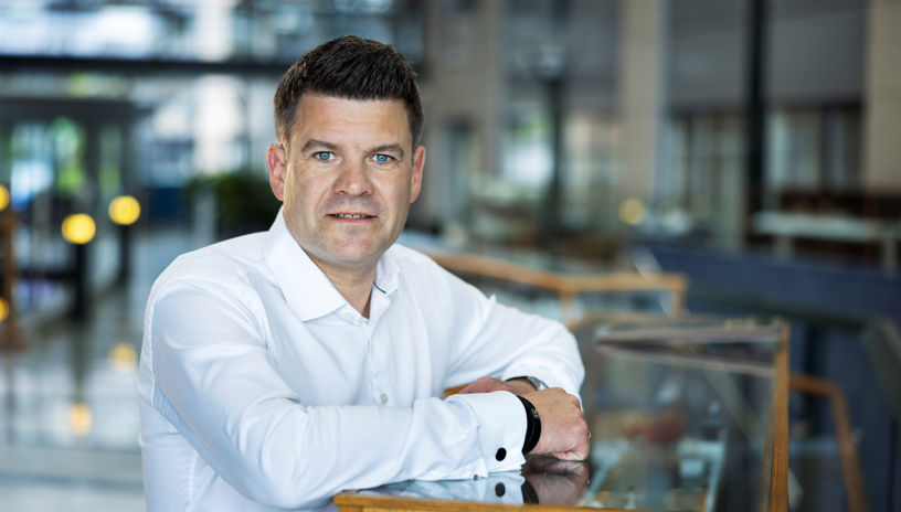 portrett av Lasse kristoffersen i hvit skjorte, lener seg på et monter med en skipsmodell 