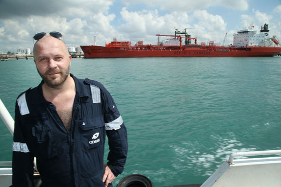 alt="port captain odd arne hansen i singapore, med det røde tankskipet bow flora i bakgrunnen"