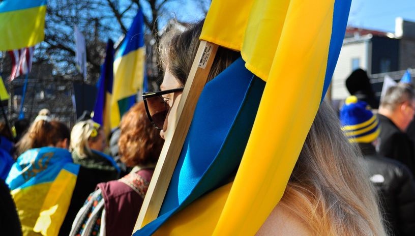 Nærbilde fra demonstrasjon for Ukraina. Mange ukrainske flagg i bakgrunnen. En blond kvinne i forgrunnen holder et ukrainsk flagg. 